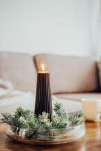 Composition Of Flaming Black Christmas Taper Candle Placed Between Spruce Branches On The Coffee Table In Living Room. Christmas Winter Still Life. Natural Christmas Decorations For Home. Vertical.