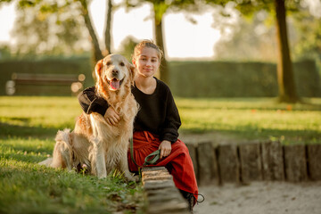 Wall Mural - Pretty girl with golden retriever dog sitting at nature and smiling. Beautiful female model teenager hugging purebred pet doggy at autumn park