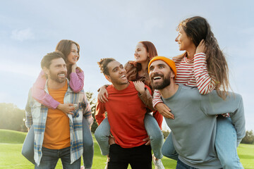 Wall Mural - Group of smiling multiracial friends, women and men carry on shoulders, playing game, having fun in park.  Diversity, friendship, meeting, positive lifestyle concept