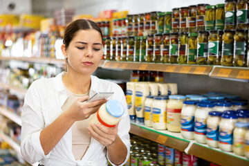 Wall Mural - Young woman looking to buy jar of mayonnaise in supermarket