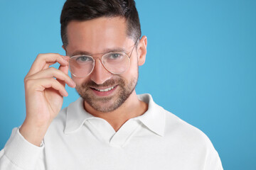 Poster - Portrait of happy man in stylish glasses on light blue background. Space for text