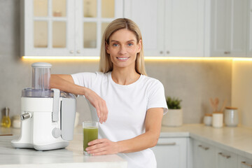 Wall Mural - Happy woman with glass of fresh celery juice at table in kitchen