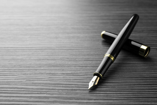 Stylish fountain pen on black wooden table, closeup. Space for text