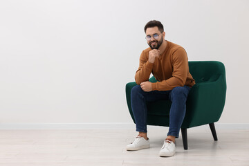 Wall Mural - Handsome man sitting in armchair near white wall indoors, space for text