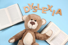 Word Dyslexia Made Of Wooden Letters, Teddy Bear And Books On Light Blue Background, Flat Lay
