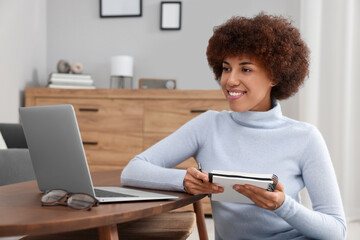 Poster - Beautiful young woman using laptop and writing in notebook at wooden coffee table in room