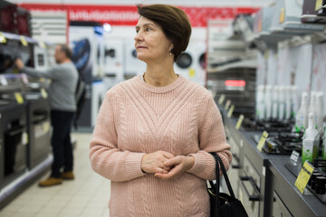 Wall Mural - Mature caucasian woman choosing gas stove in appliance store.