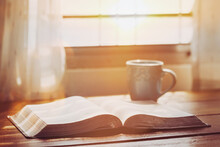 Close Up Of An Open Bible With A Cup Of Coffee For Morning Devotion On Wooden Table With Window Light Effected With Copy Space For Text