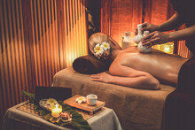 Hot Herbal Ball Spa Massage Body Treatment, Masseur Gently Compresses Herb Bag On Woman Body. Tranquil And Serenity Of Aromatherapy Recreation In Warm Lighting Of Candles At Spa Salon. Quiescent