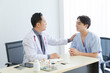 © aekkorn - Male doctor and young male patient while consult and explain. Doctor and patient sitting together  at table in clinic.