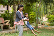 © WESTOCK - focus on mother, Cheerful indian mother playing by rotating his daughter at park - concept of weekend holidays, Carefree moments and Playful affection.