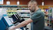 © kalafoto - A person uses a self-checkout device in a supermarket