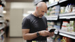 © kalafoto - A man uses her smartphone to check his purchase list in a supermarket