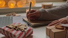 Young Woman Writing Christmas Cards, Makes Order On Laptop. Female Picking Gifts Online Purchases At Cozy Home Among Gift Boxes And Packages. Winter Sales, Black Friday. Christmas Discount Promotions	