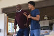© Wavebreak Media - Happy african american adult son helping senior father stand up from couch at home