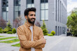 © Liubomir - Successful Hindu man standing outside office building with arms crossed, smiling and looking away.