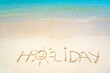 Holiday hand written in the sand on the beach blue waves in the background. Sun drawing on golden sand beach, holiday background sign concept.