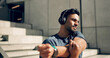 © N Felix/peopleimages.com - Fitness, headphones and man stretching arms on stairs in city, workout and exercise for body health. Music, serious athlete and person warm up on steps in urban town, listening to audio and thinking