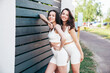 Two young beautiful smiling female in trendy summer white cycling shorts and top clothes. Sexy carefree women posing in street at sunny day. Positive models having fun. Cheerful and happy. Near fence