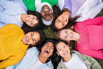 Wall Mural - Multiracial group of young women in circle smiling at camera together - Happy girlfriends having fun lying on the grass at the park - Female community and friendship concept - Women power