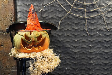 a large pumpkin with a carved scary face in a witch hat on a background of a gray wall with a cobweb and spiders, a decoration for the Halloween holiday