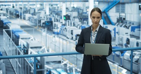 Poster - Portrait of a Caucasian Female Engineer Using Laptop Computer and Looking Around a Factory Facility with Robotic Arms Producing Modern Electronic Components for Tech Industries