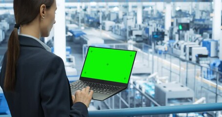 Aufkleber - Young Female Engineer Using Laptop Computer with Green Screen Mock Up Display at an Electronics Factory. Over the Shoulder Footage. Automated Manufacturing Machines and AI Robots Are Monitored Online