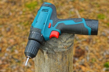 electric modern portable battery-powered hand-held convenient blue plastic  for working in the house screwdriver tool  lies on the wooden stump on the street  