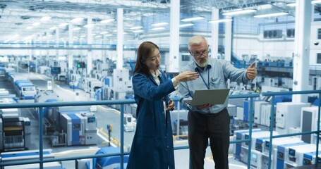 Fototapete - Portrait of a Middle Aged Engineer and Positive Asian Scientist Using Laptop Computer and Talking in a Factory Facility with Equipment Producing Modern Electronic Components for Different Industries