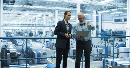 Fototapete - Male and Female Engineers Standing at a Plant, Using Laptop Computer and Talking in a Factory Facility with Equipment Producing Modern Electronic Components for Different Industries
