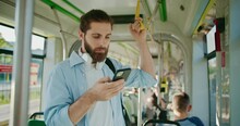 Male Young Traveler With Backpack Using Smartphone To Surfing Internet Or Scrolling Social Networks. Handsome Guy Riding In Public Transport, Standing Inside Bus And Recording Voice Messages.