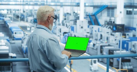 Fototapete - Technician Using Laptop Computer with Green Screen Chromakey Mock Up Display and Looking Around a Factory Facility with Modern Machines Producing Electronic Components for Tech Industries
