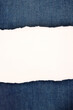 Torn piece of light colored blank paper for your own text on blue jeans background.