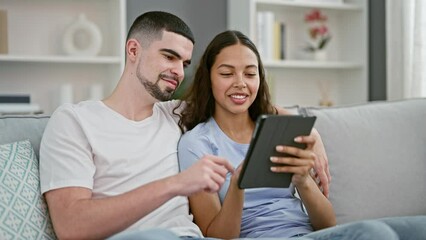 Wall Mural - Smiling beautiful couple enjoying technology together at home, casual lifestyle of confident man and woman sitting on sofa, using touchpad