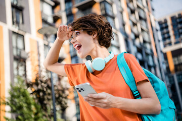 Poster - Photo of sweet excited girl dressed orange t-shirt eyewear backpack looking route modern gadget app outdoors urban town park