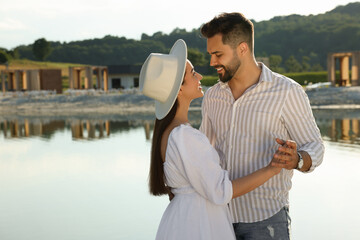 Wall Mural - Romantic date. Beautiful couple spending time together near lake, space for text