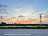 Fototapeta Na sufit - Thailand road with electricity poles, green fields, and a beautiful sunset.