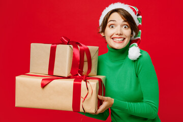 Wall Mural - Young fun surprised woman wear green turtleneck Santa hat posing hold many present boxes with gift ribbon bow look aside isolated on plain red background Happy New Year 2024 Christmas holiday concept