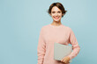 Young fun smiling happy IT woman she wears beige knitted sweater casual clothes hold closed laptop pc computer isolated on plain pastel light blue cyan background studio portrait. Lifestyle concept.