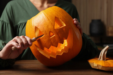 Wall Mural - Woman carving pumpkin for Halloween at wooden table, closeup