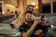 © Marko Geber - Gay couple sharing a tender moment while taking a selfie on the couch
