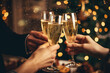 © colnihko - Happy friends having fun and toasting sparkling wine glasses close-up against golden bokeh lights background. Christmas celebration