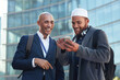 Phone, city and diversity business men for global networking, social media update and corporate collaboration. Happy black man with Arab, muslim or islamic partner on smartphone of international chat