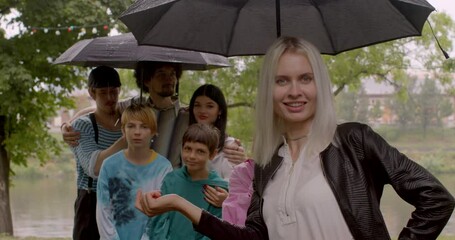 Wall Mural - A group of joys pose under an umbrella in rainy weather. Blonde woman touches an umbrella, smiles. Positive mood in a friendly company.