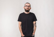 © satura_ - Portrait of attractive handsome man millennial with beard who looks into camera on isolated simple background and wears black t-shirt from premium organic materials