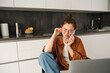 Image of lovely young woman at home, calling someone, sitting with mobile phone, talking on smartphone and smiling