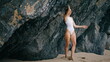 Woman standing sand seacoast raising hands to rock. Hot model posing on beach.