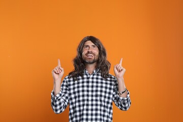 Wall Mural - Hippie man pointing upwards on orange background