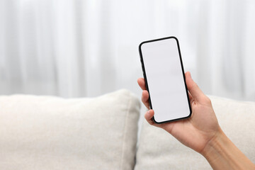 Woman holding smartphone in hand at home, closeup. Space for text