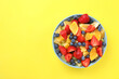 canvas print picture - Yummy fruit salad in bowl on yellow background, top view. Space for text